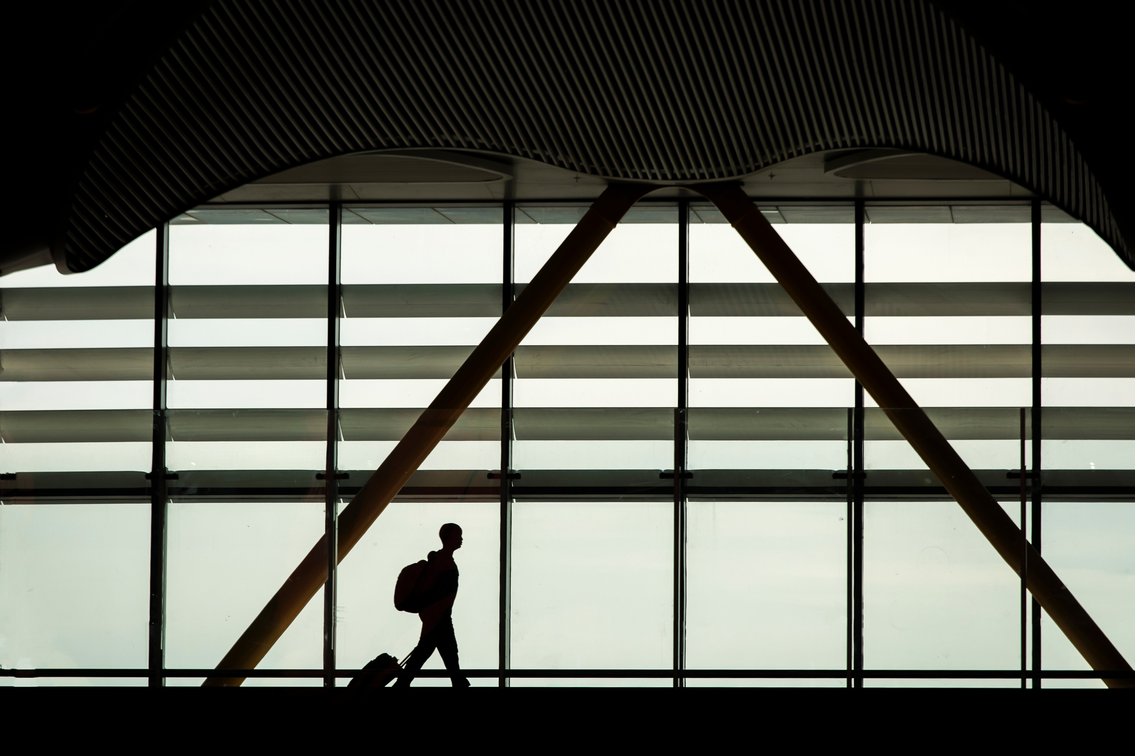 Silhouette von Mann mit Koffer und Rucksack vor Flughafenfensterfront; Duisburg Wirtschaftsdetektei, Duisburg Wirtschaftsdetektiv, Duisburg Privatdetektiv, Duisburg Privatermittler