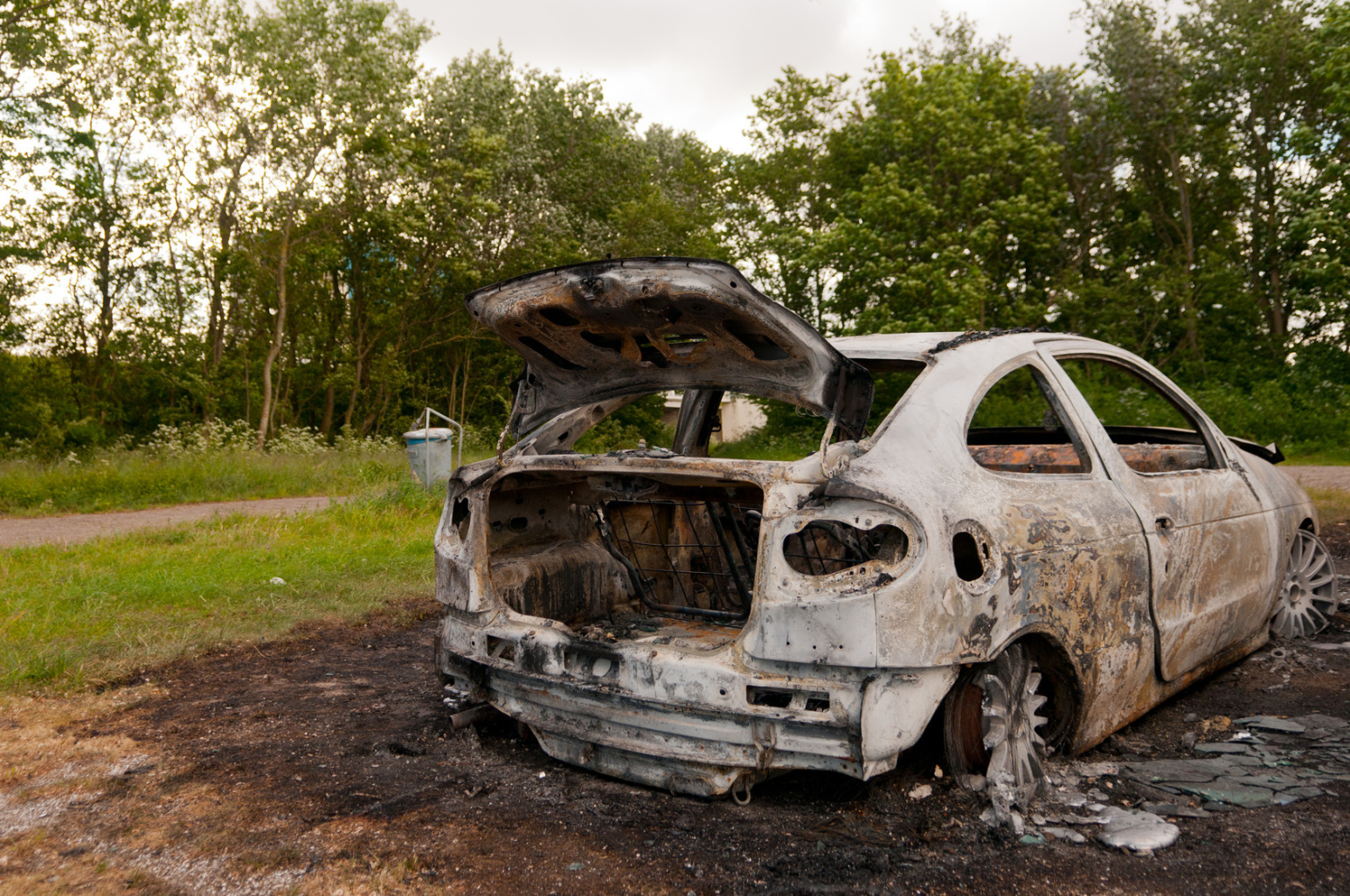 Ein ausgebrannter weißer 2-Türer auf einer Wiese, vermutlich Opel; Detektive der Kurtz Detektei Duisburg